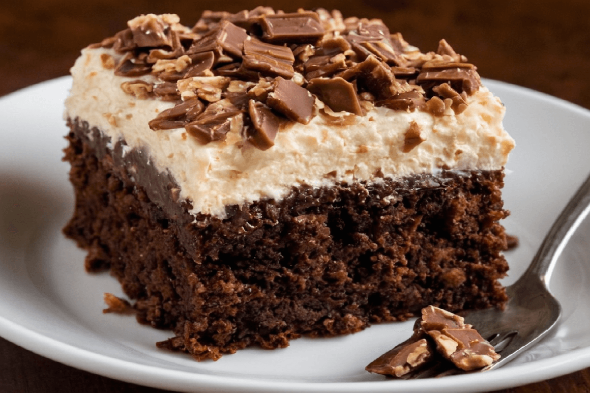 A slice of German Chocolate Poke Cake with chocolate ganache and coconut pecan frosting, served on a white plate with a fork.